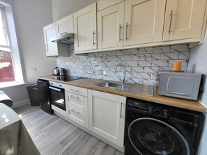 A compact kitchen with white cabinets, a marble backsplash, a dishwasher, a washing machine, and a toaster. - Top Location - Newly Refurbed 2BD, Sleeps 6 W/Loft (Cork)