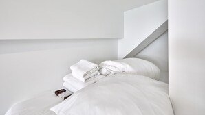 Un lit bien fait, avec des draps blancs et une serviette pliée, un oreiller blanc et une petite bouteille posée à côté.