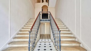 Un grand escalier, dont le sol est recouvert d’un motif en damier noir et blanc, mène à une porte située en haut.