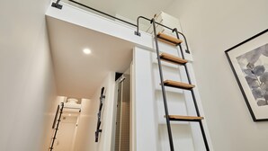 Une salle de bain moderne avec une douche, une porte blanche et un escalier menant à une mezzanine.