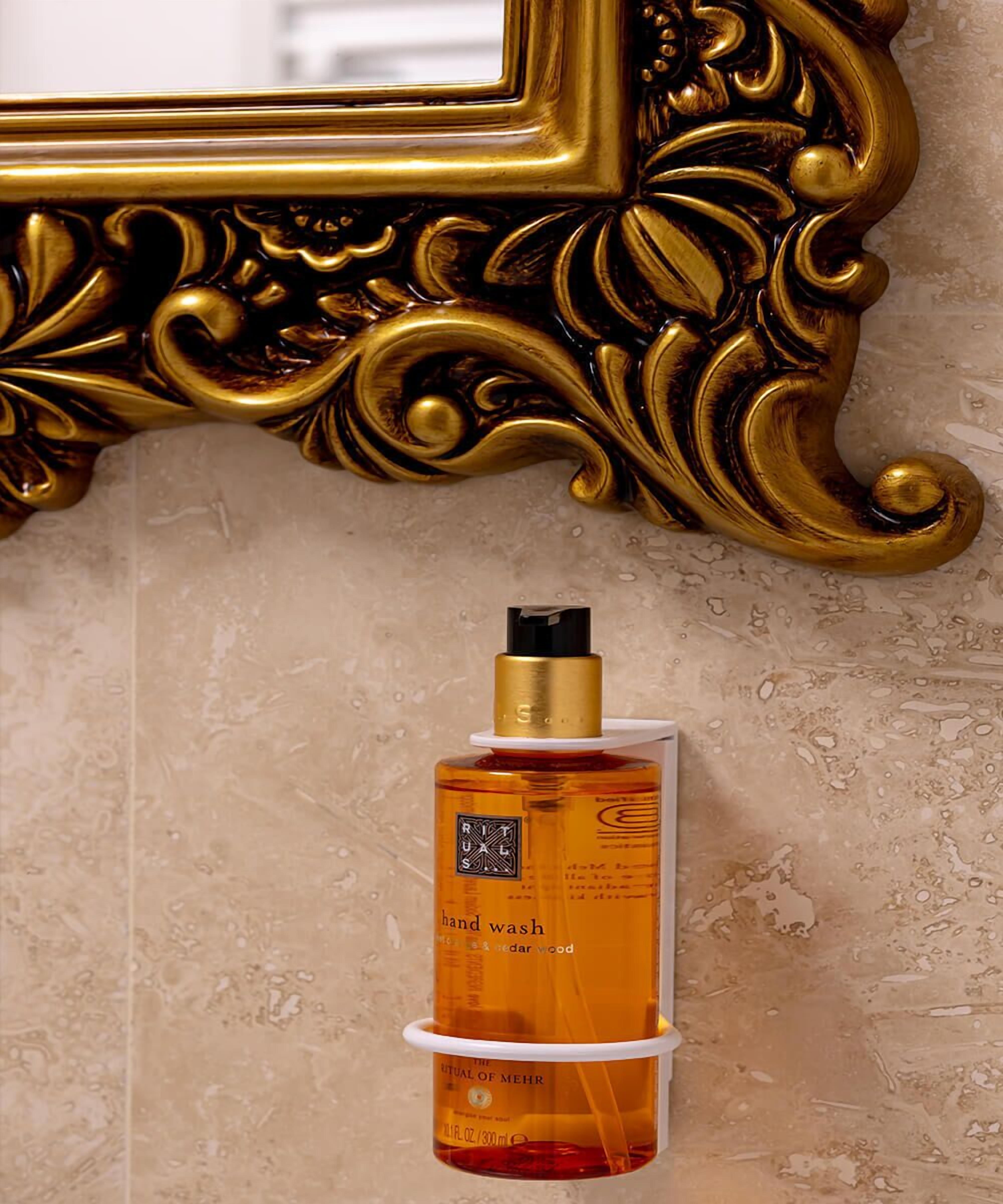 A hand wash bottle labeled "RITUALS" with a gold cap, mounted on a textured beige wall.