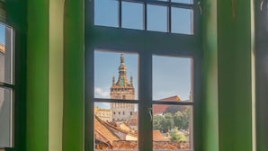 A room with a large arched window overlooking a historic building with a tower. - Heritage Boutique Hotel Sighisoara (Sighişoara)