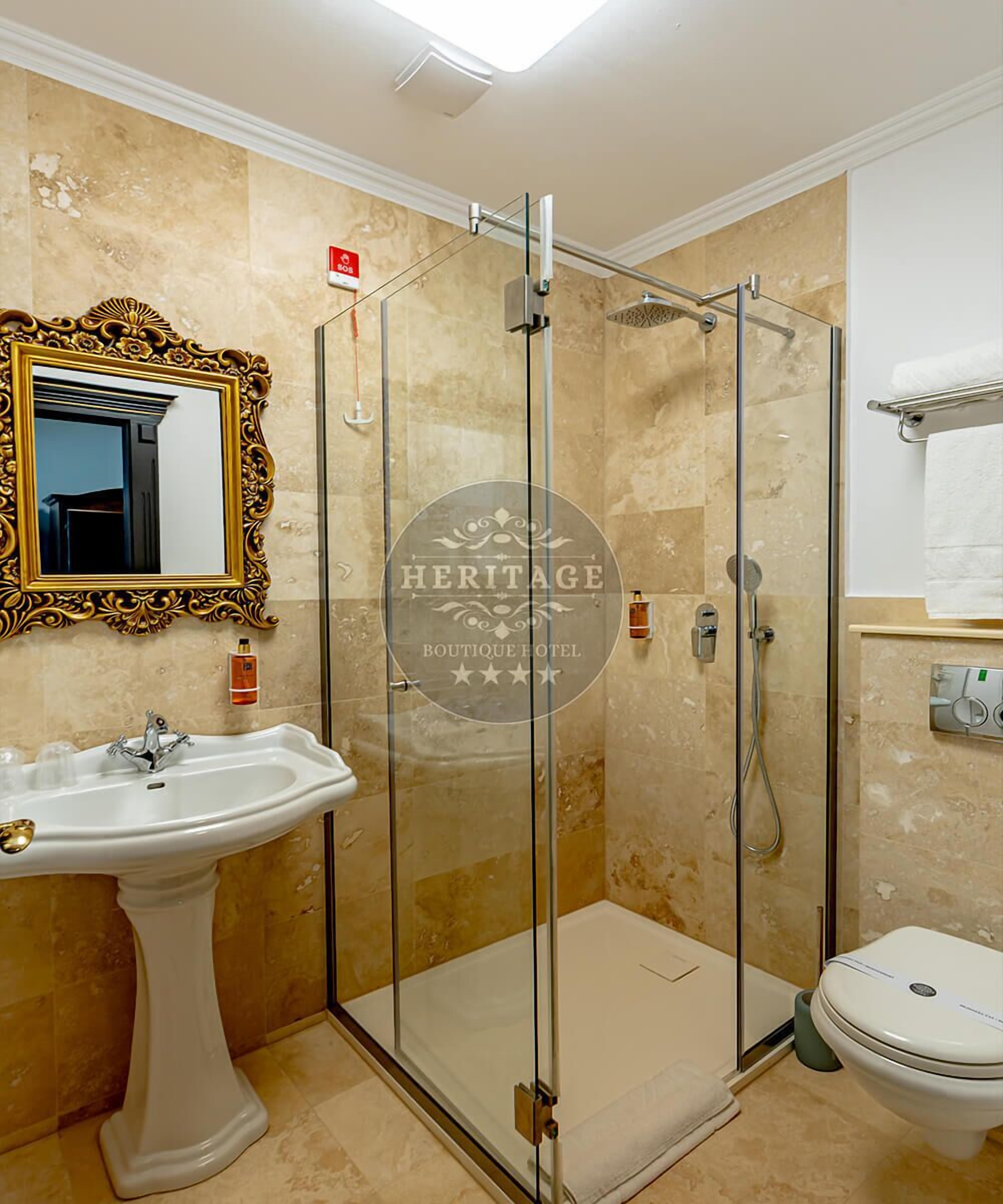 A bathroom with a glass-enclosed shower, a pedestal sink, a toilet, and a mirror with an ornate frame.