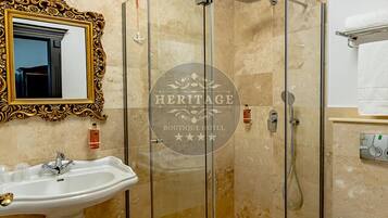 A bathroom with a glass-enclosed shower, a pedestal sink, a toilet, and a mirror with an ornate frame.
