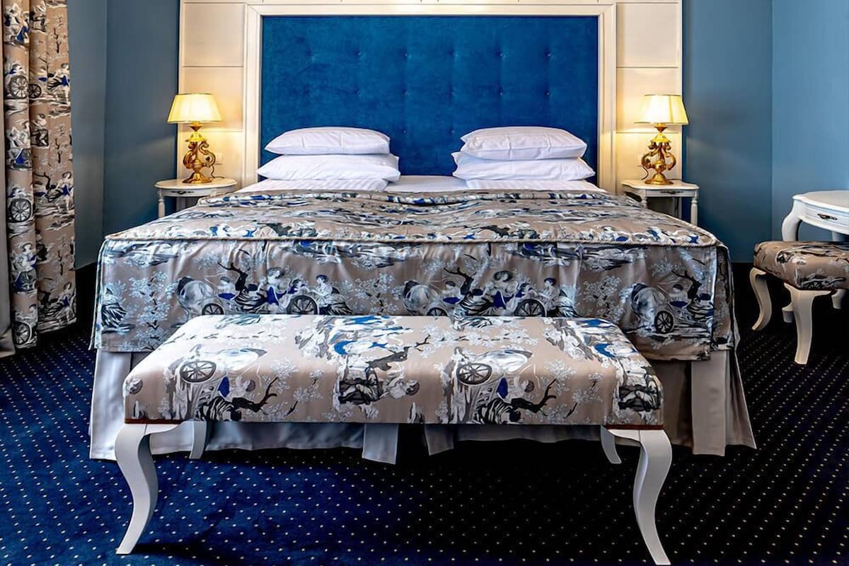 A bedroom with a large bed, two bedside lamps, a chandelier, and a blue headboard.
