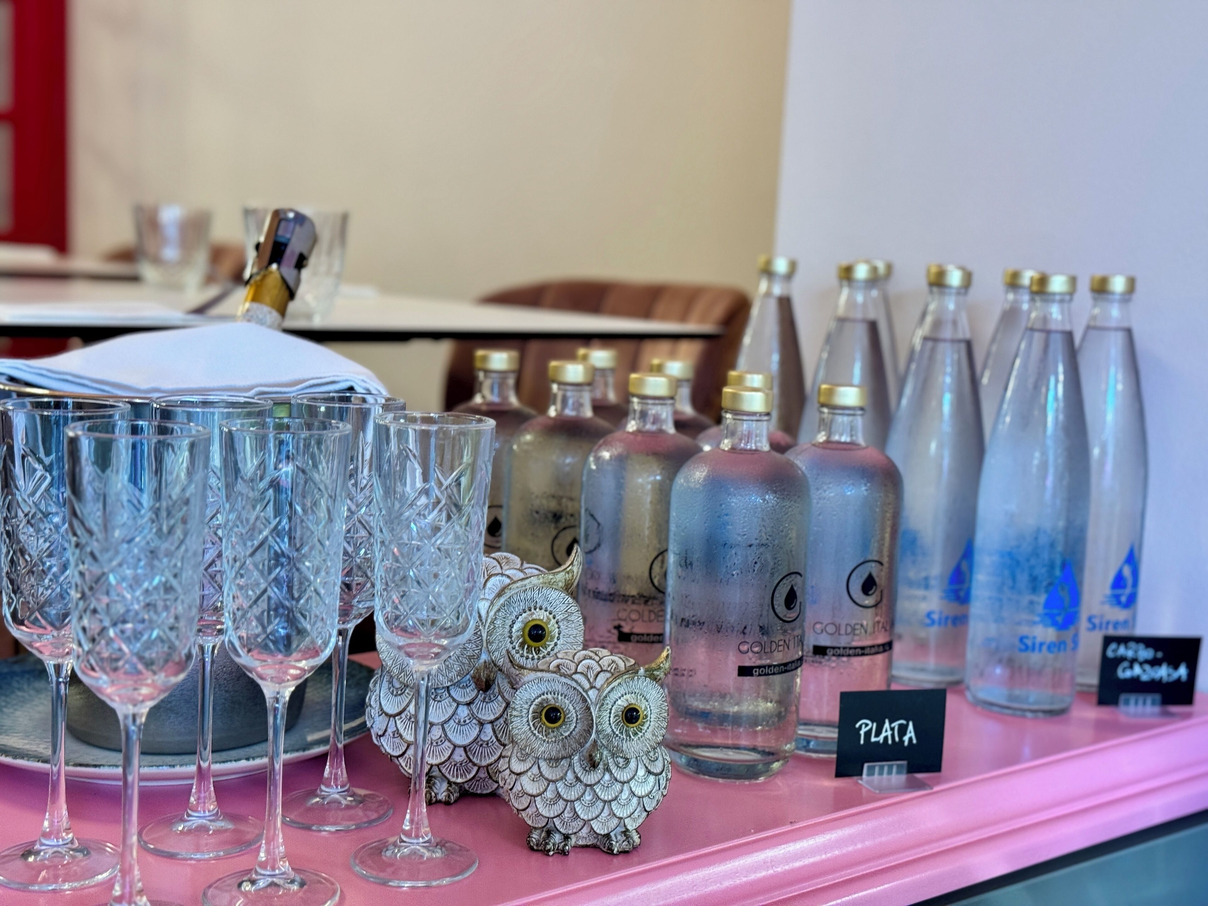 A display of various glassware and bottles on a pink shelf.