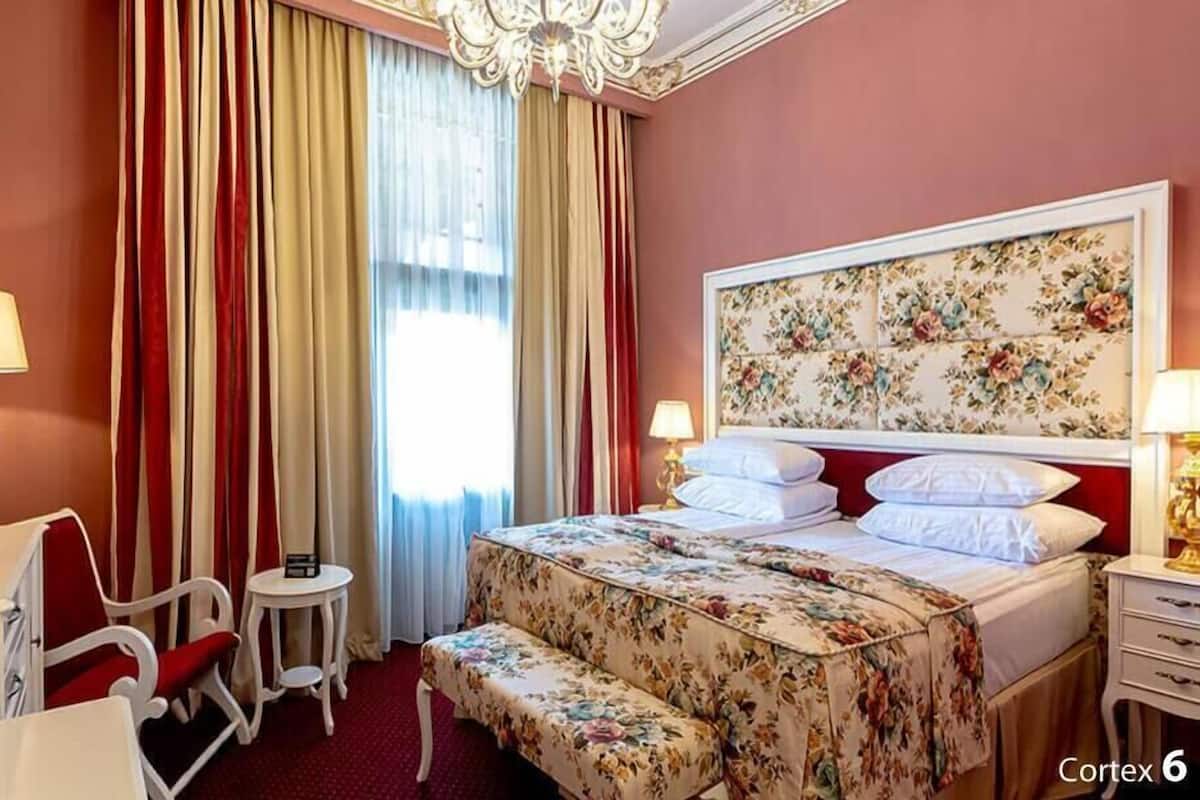 A hotel room with a bed, a desk, a chair, a small table, and a chandelier.