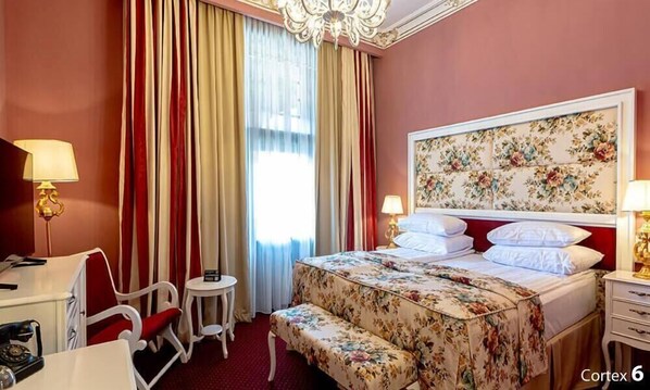 Quarto de hotel com cama, escrivaninha, cadeira, mesinha e lustre.