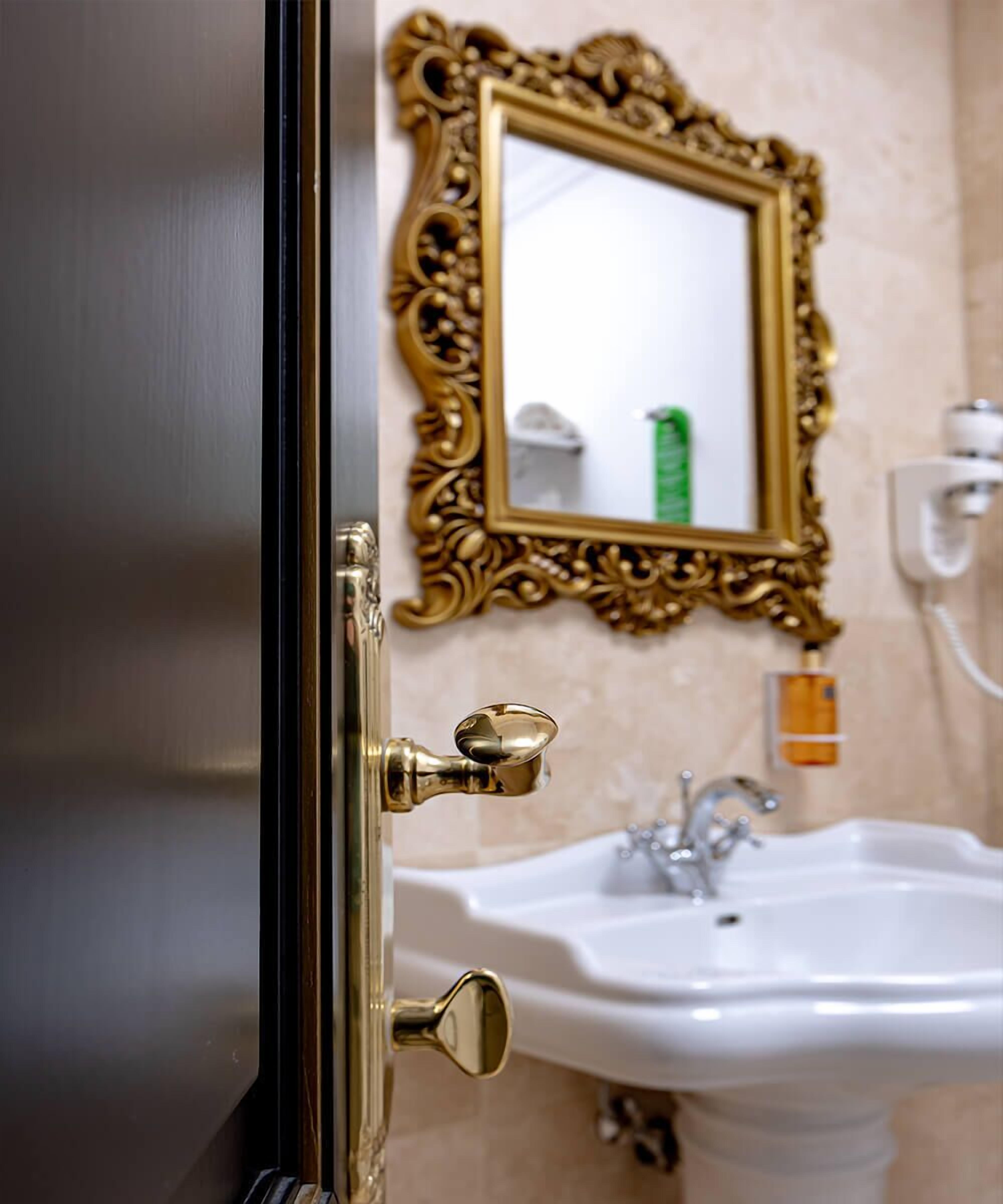 A bathroom with a gold-framed mirror, a white sink, and a door with a brass handle.