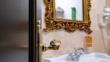 A bathroom with a gold-framed mirror, a white sink, and a door with a brass handle.