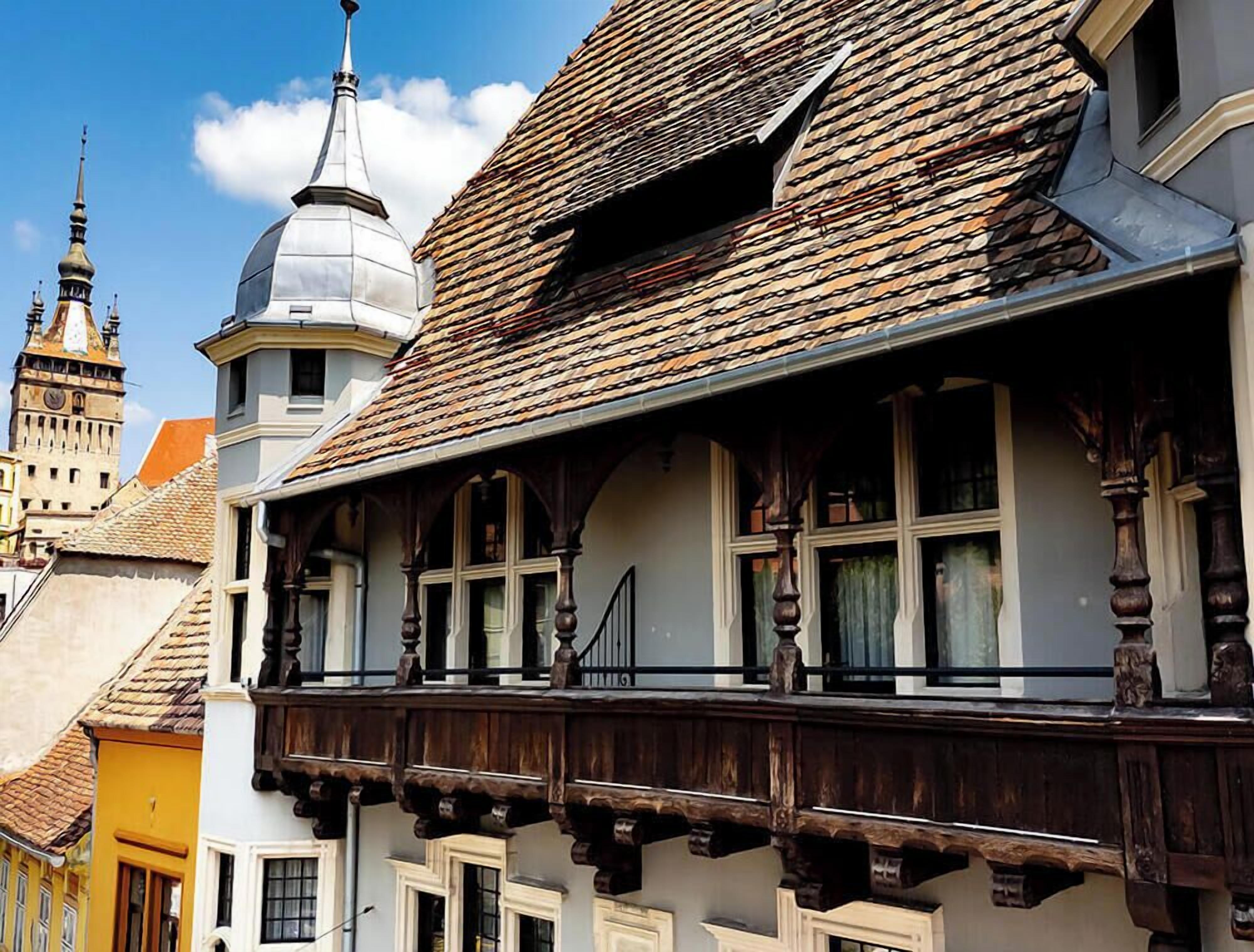 Een klassiek gebouw met balkon, een klokkentoren op de achtergrond en een koepelstructuur.