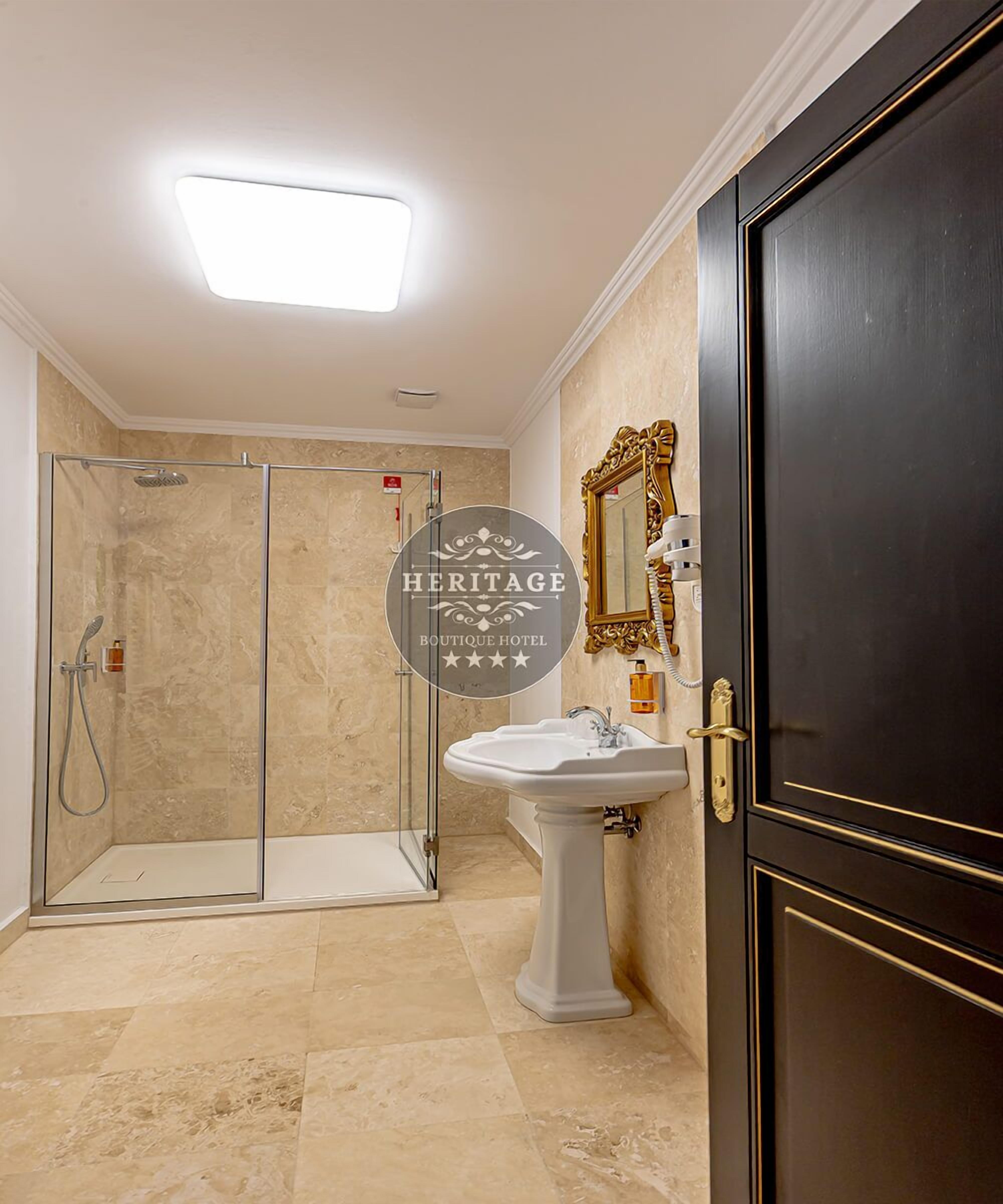Un baño con cabina de ducha de vidrio, lavamanos pedestal y puerta de madera oscura.