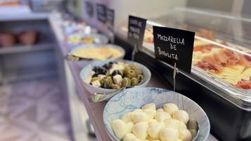 Un bufé con diversas opciones de comida, incluyendo un bol de aceitunas, un bol de queso mozzarella y una bandeja de embutidos cortados.