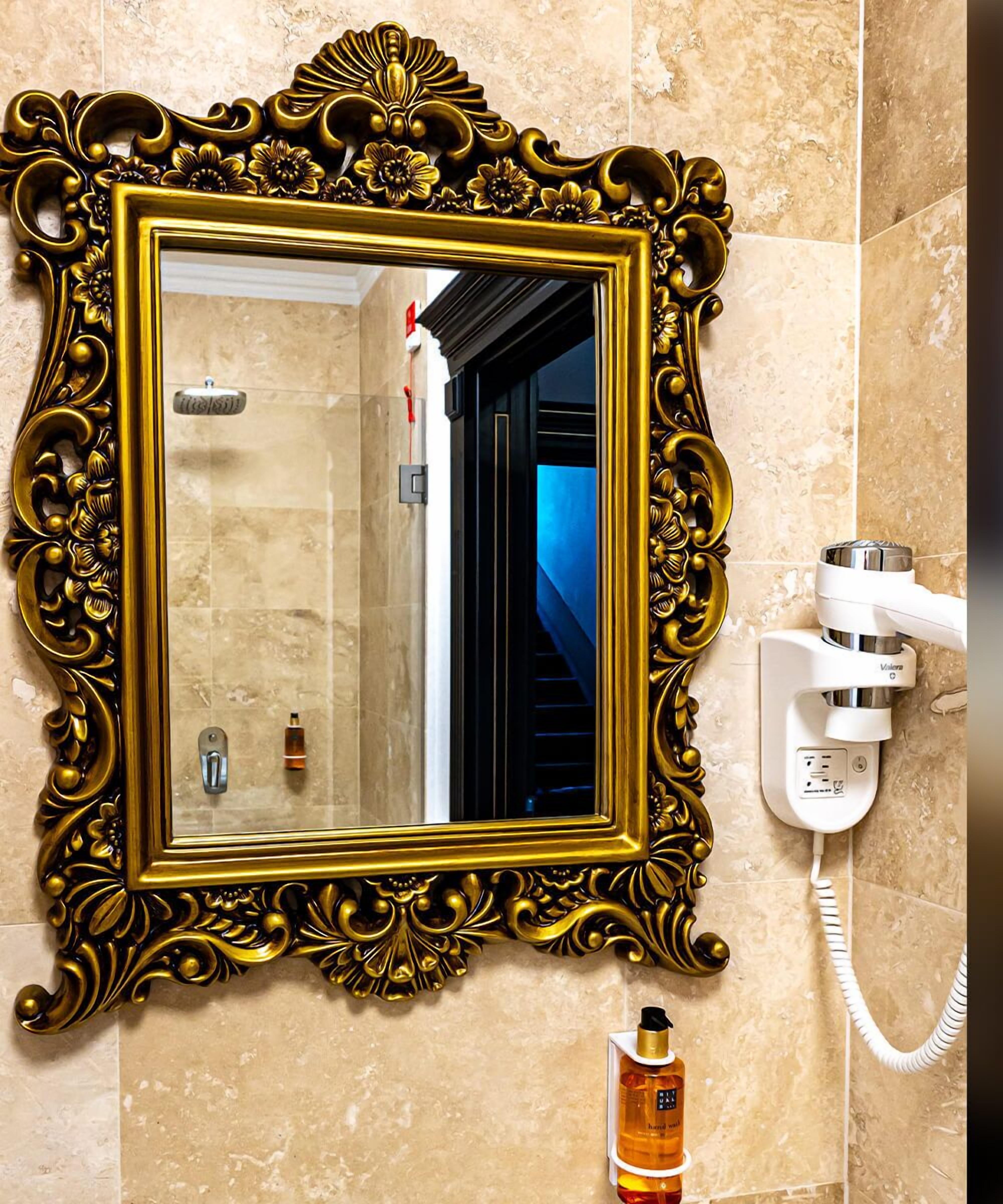 A bathroom with a gold-framed mirror, a white telephone, and a bottle of hand soap.