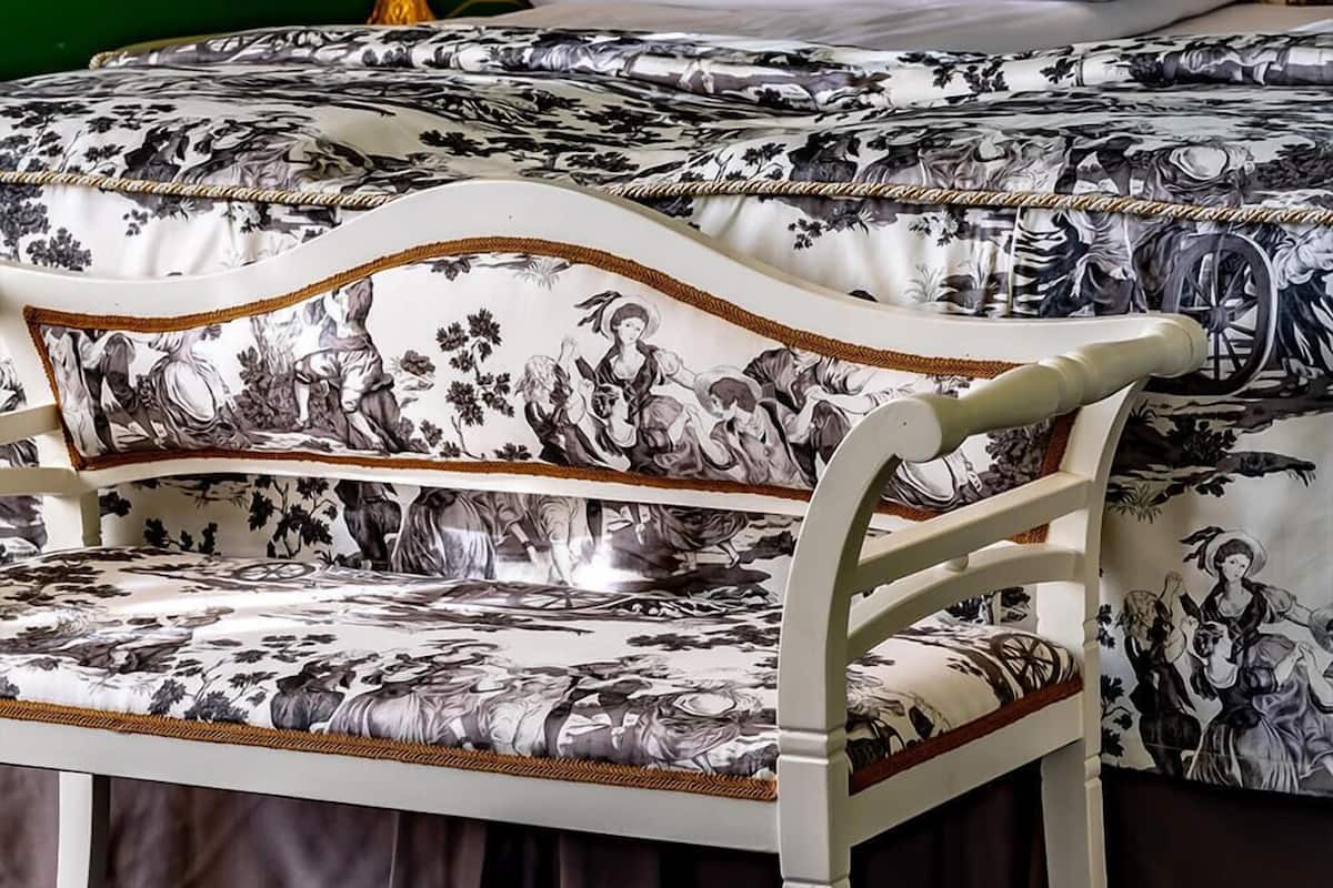A bed with a floral-patterned bedspread, a white pillow, and a gold lamp beside it.