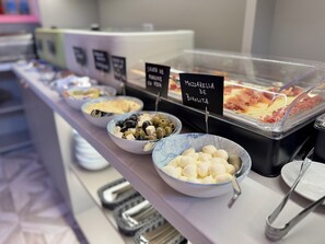 Un bufé con platos identificados, incluyendo mozzarella y aceitunas.