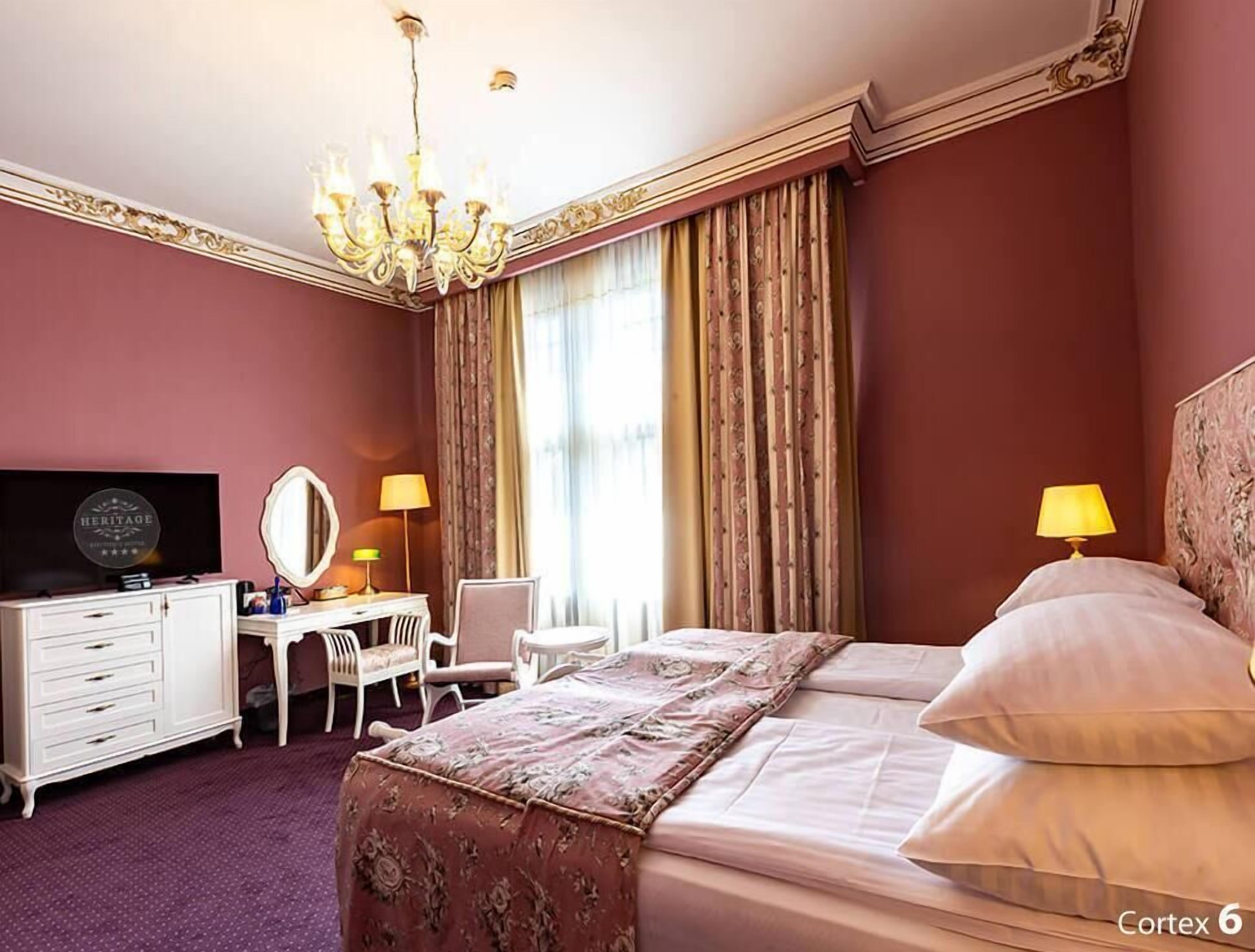 A hotel room with a bed, a desk with a chair, a vanity with a mirror, and a chandelier.