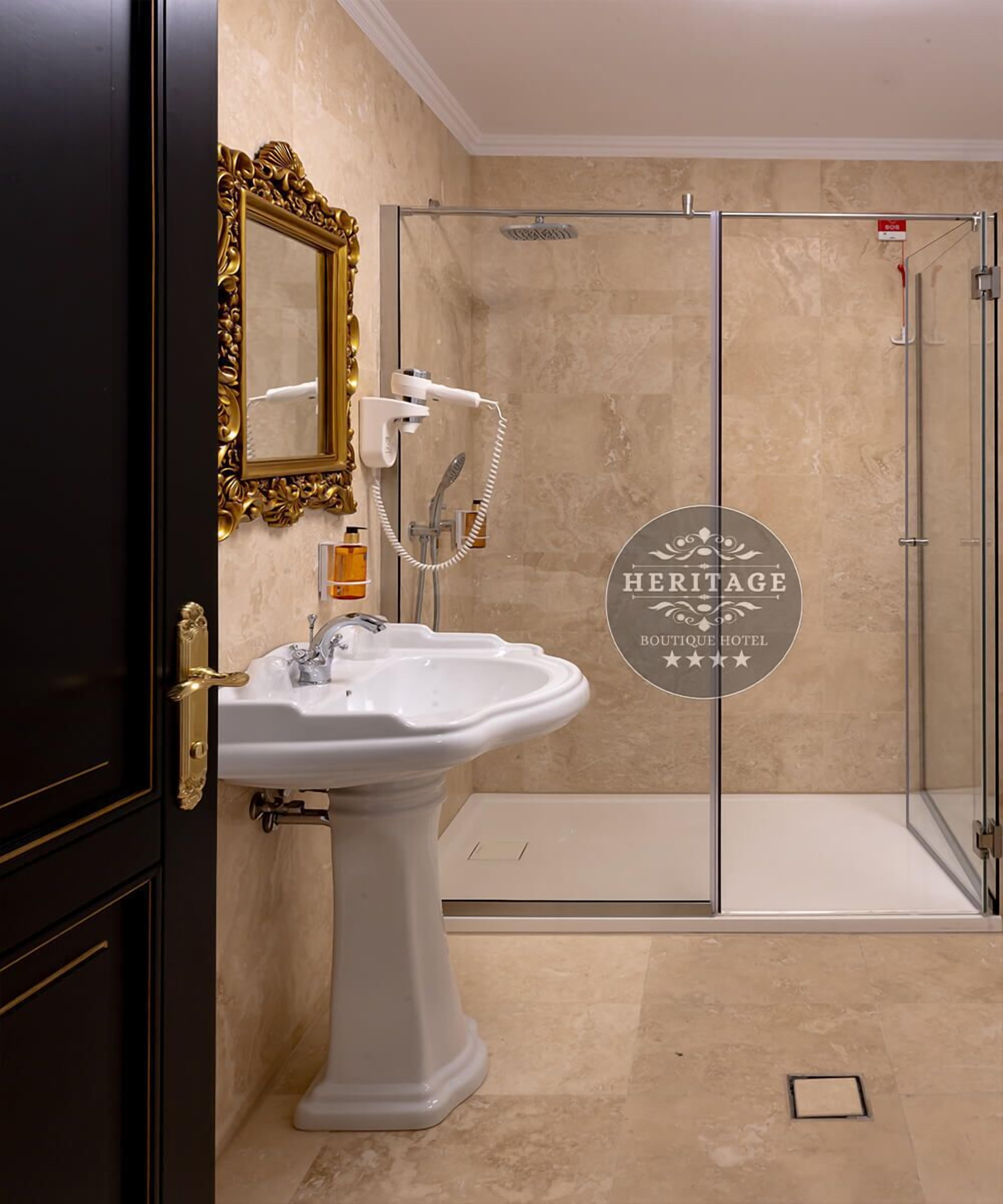 A bathroom with a pedestal sink, a glass shower enclosure, and a gold-framed mirror.