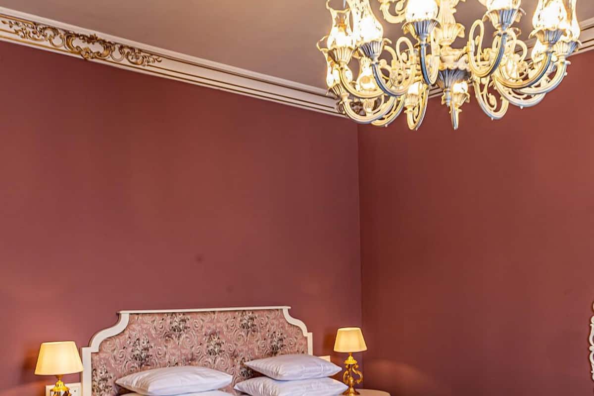 A bedroom with a large bed, two bedside tables with lamps, and a chandelier.