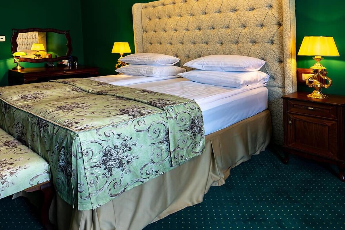 A bedroom with a large bed, green walls, a chandelier, and two bedside lamps.