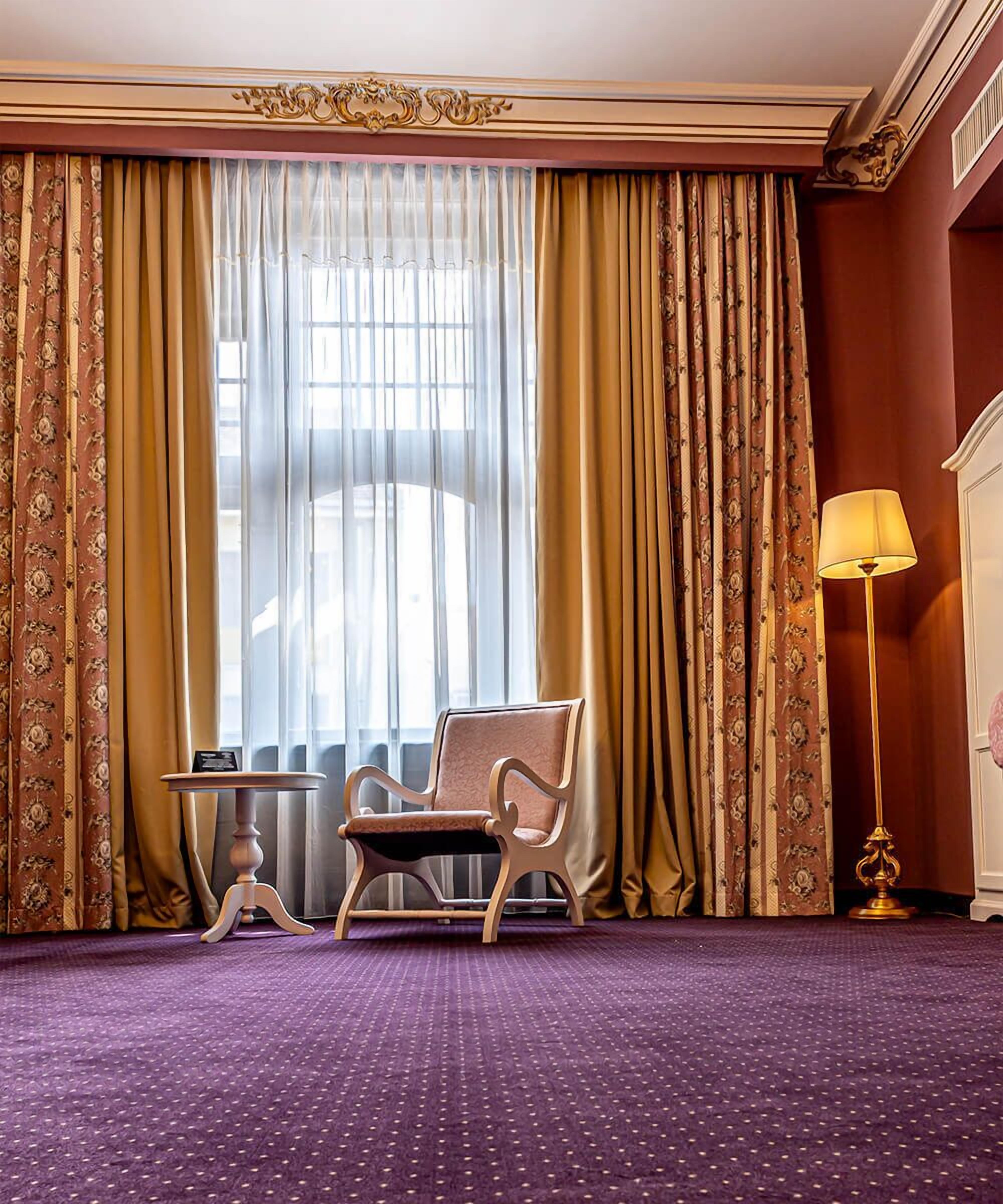 Une pièce avec une grande fenêtre, une chaise, une table et une lampe.