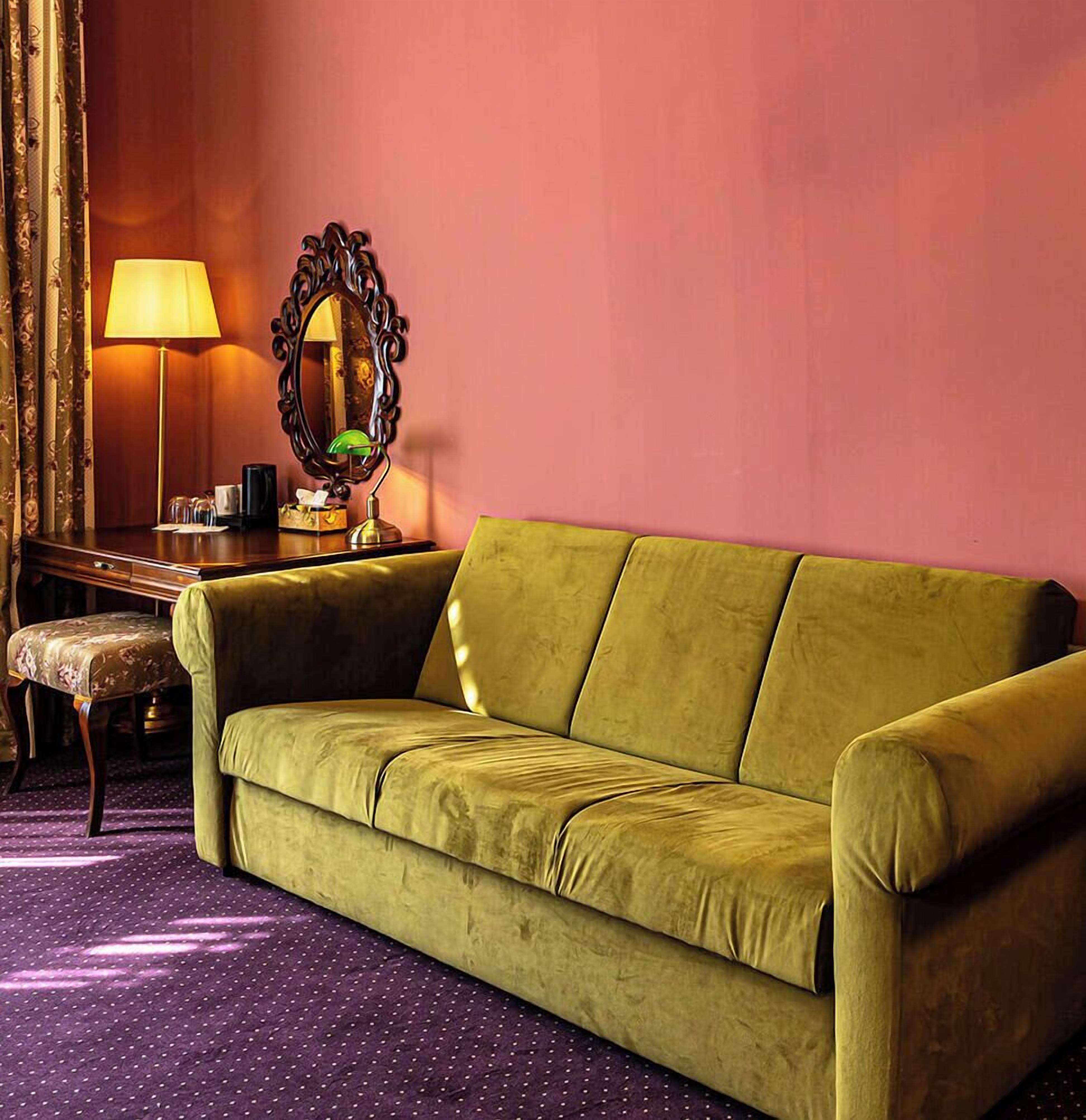 Un sofá verde en una habitación con alfombra morada, un escritorio de madera, una lámpara y un espejo.