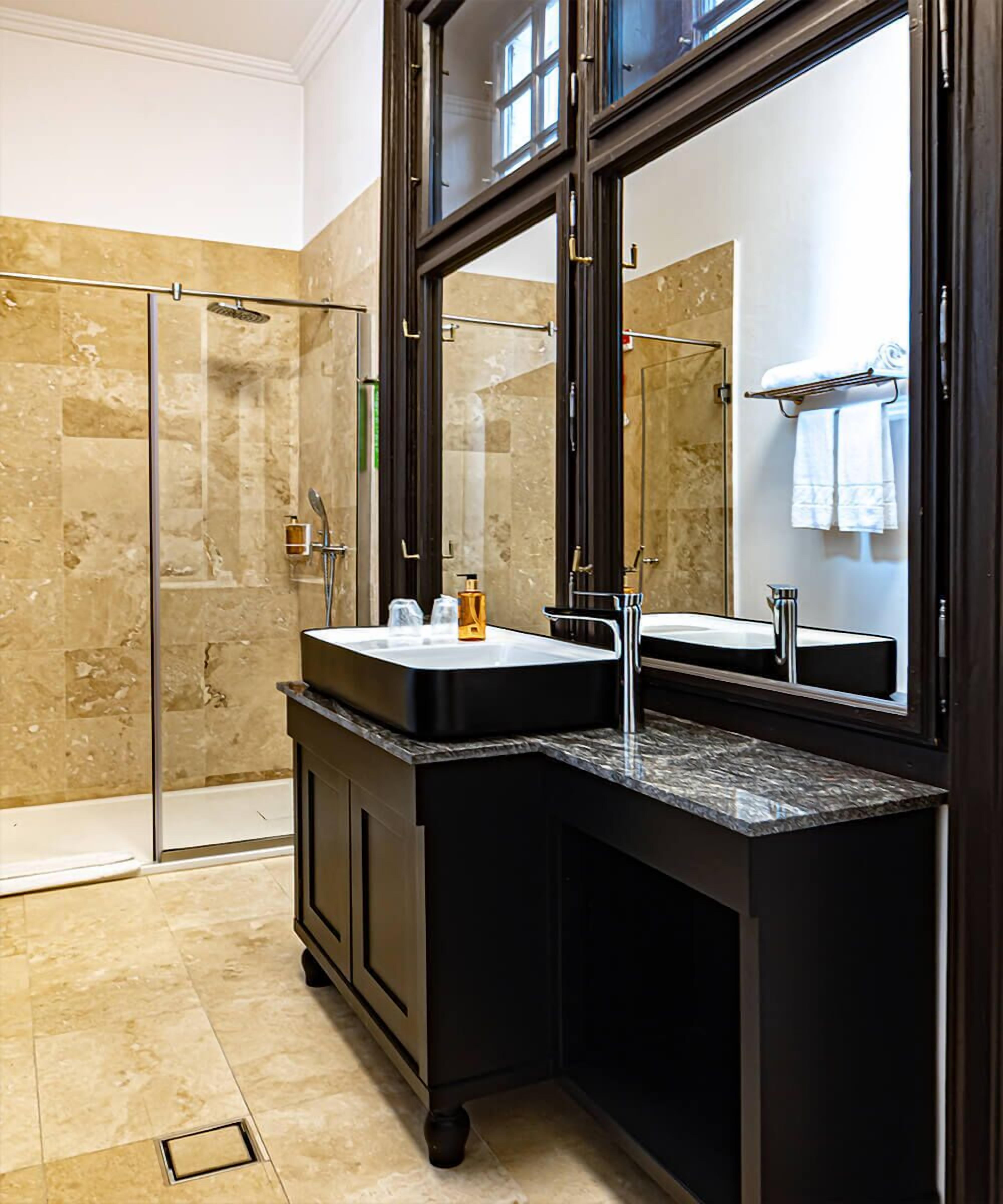A modern bathroom with a glass shower enclosure, a black vanity with a sink, and a large mirror.