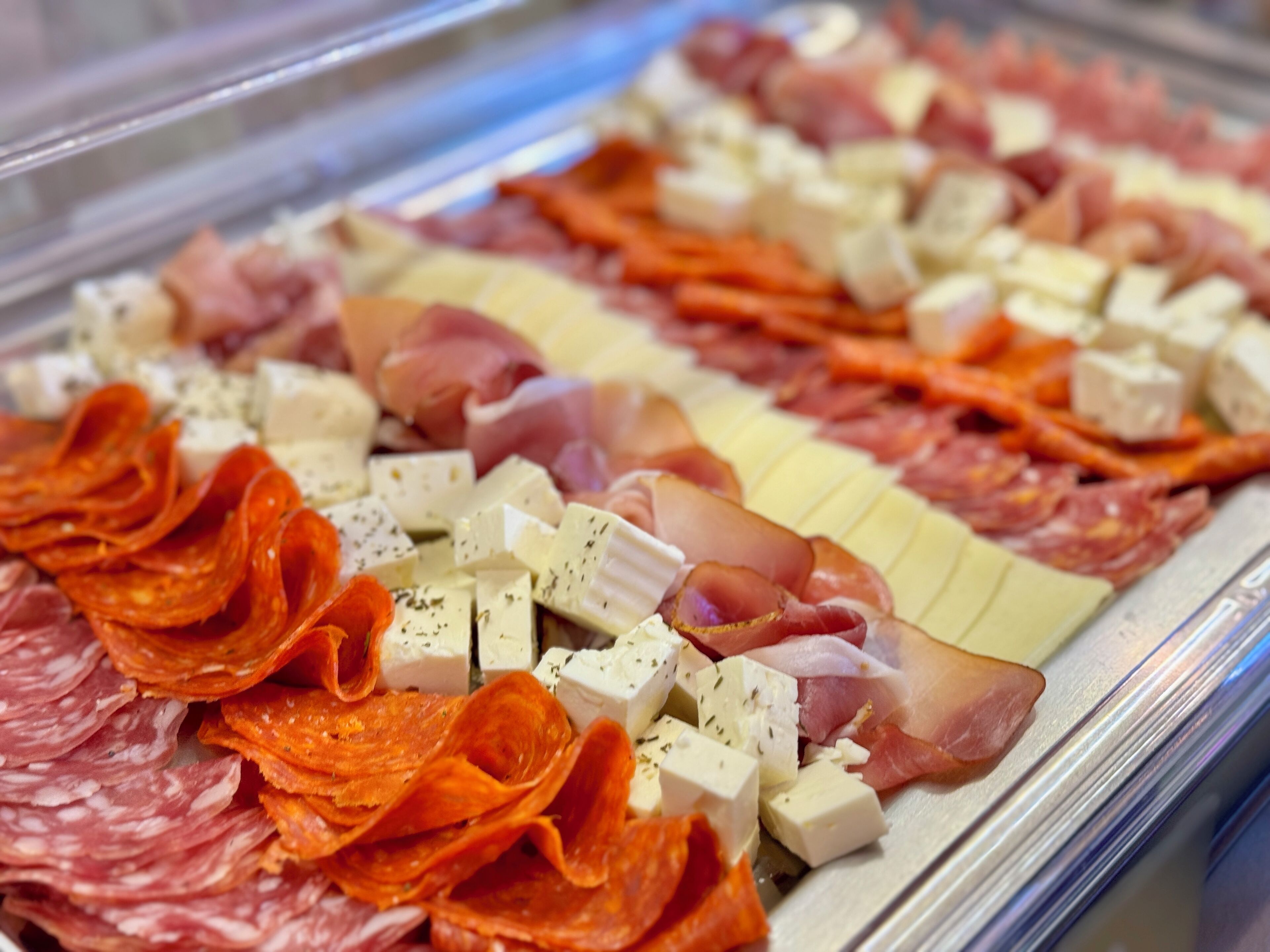 Una exhibición de diversos embutidos y quesos en una vitrina de delicatessen.