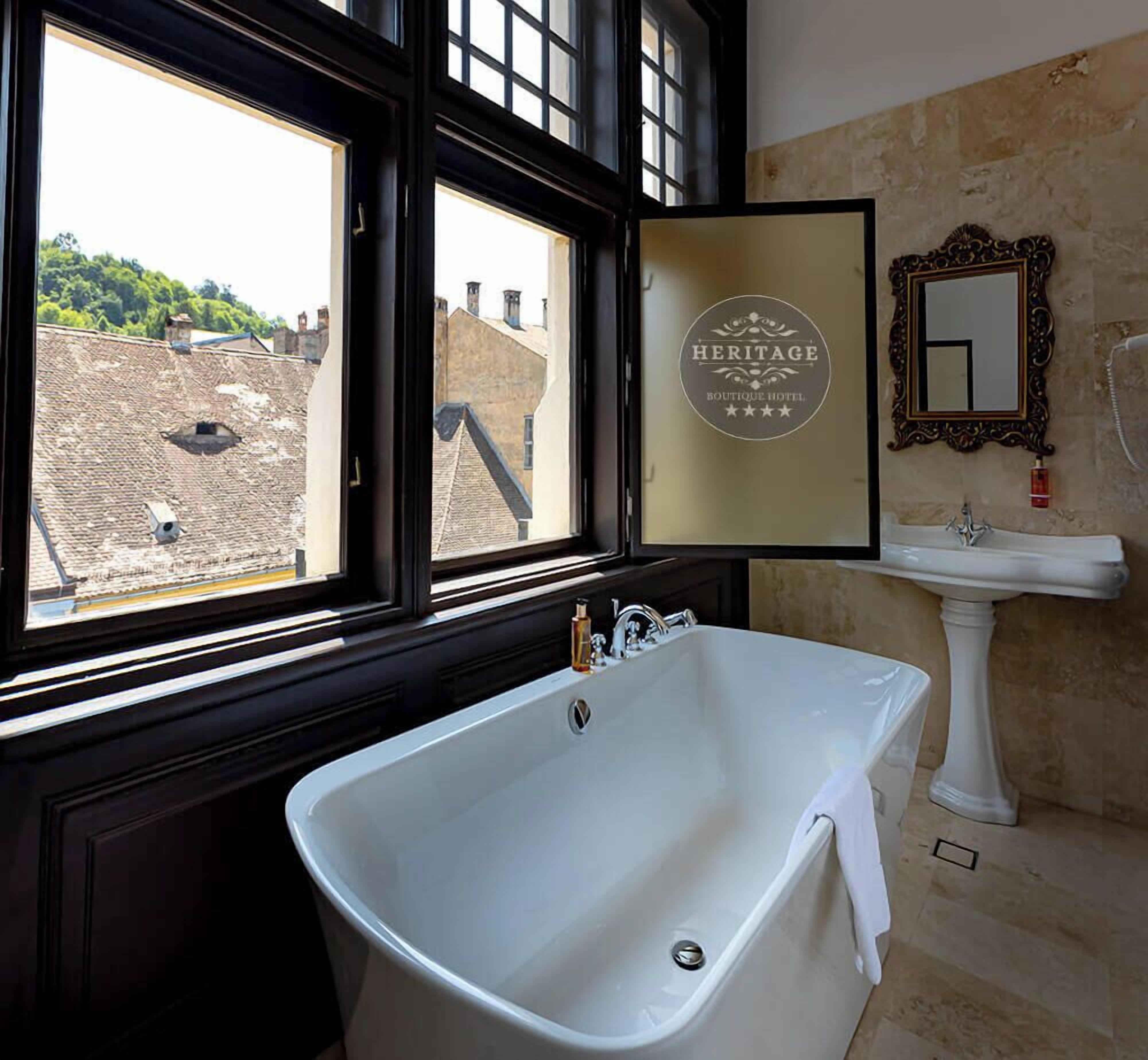 Un bagno con una vasca da bagno indipendente, un lavandino e uno specchio. Una finestra offre vista sugli edifici esterni.