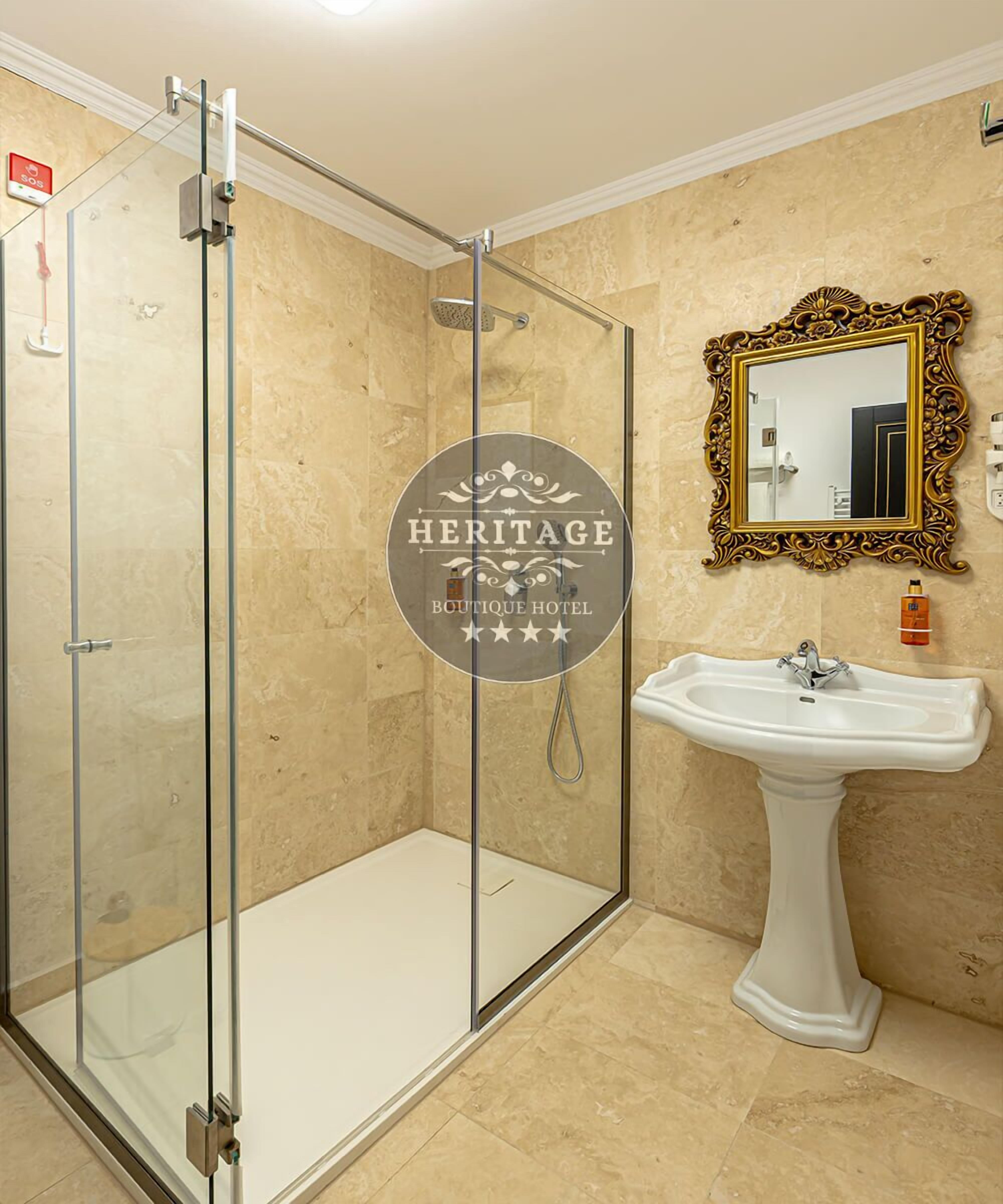 A bathroom with a glass-enclosed shower, a pedestal sink, and a decorative mirror.