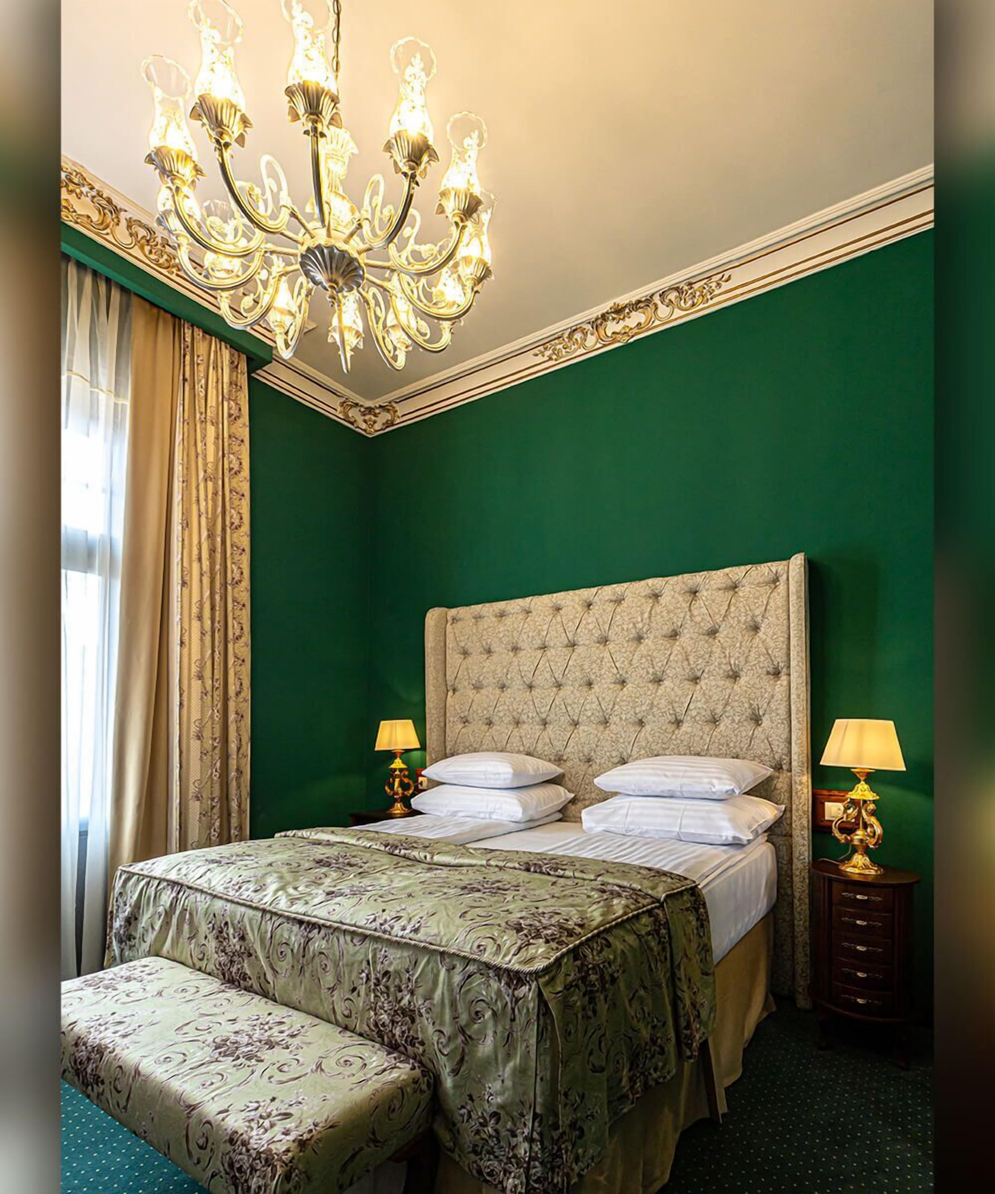 Camera da letto con testiera trapuntata, un letto grande con lenzuola bianche, due lampade da comodino e una panca imbottita verde.