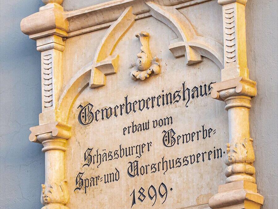A carved stone plaque with text and architectural details, including a lion's head and columns.