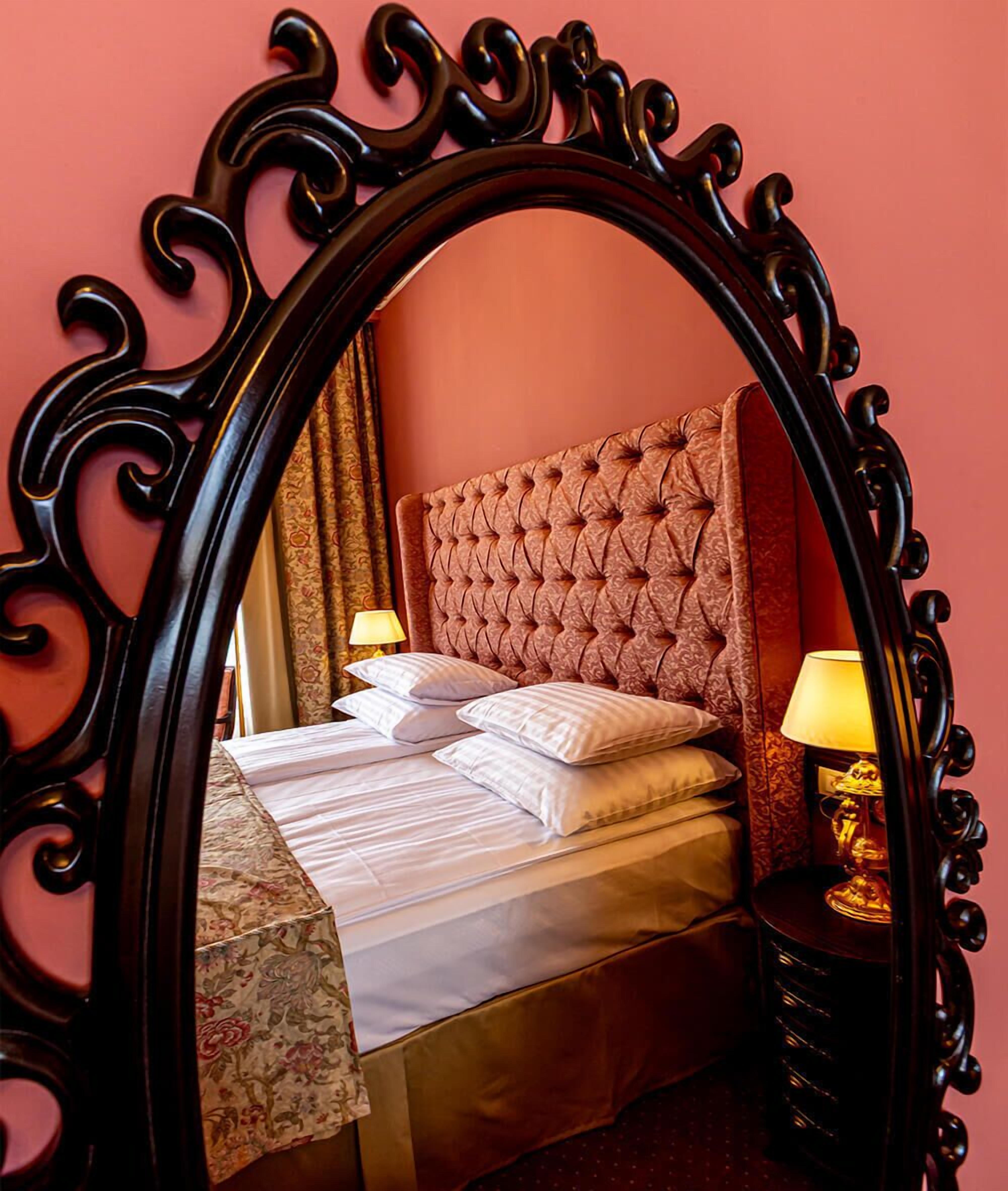 A bed with a tufted headboard, a bedside table with a lamp, and a mirror with ornate detailing.