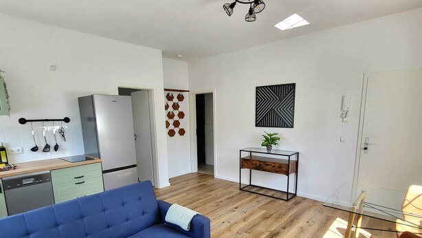 A modern living space with a blue sofa, a glass coffee table, and a wooden dining table. - 2-room apartment 1 - Apartments am Schloss (Oberschleißheim)