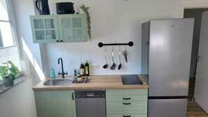 A compact kitchen with a dishwasher, a refrigerator, a sink, and a wooden countertop. - 2-room apartment 1 - Apartments am Schloss (Oberschleißheim)
