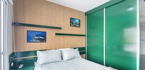Un dormitorio con cama, dos cuadros en la pared, un armario verde y un teléfono en la mesita de noche.