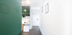 Un pasillo estrecho con una zona de cocina a la izquierda, una puerta blanca al final y cuadros en la pared derecha.