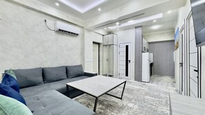 A modern living room with a sectional sofa, a coffee table, and a flat-screen TV mounted on the wall.
