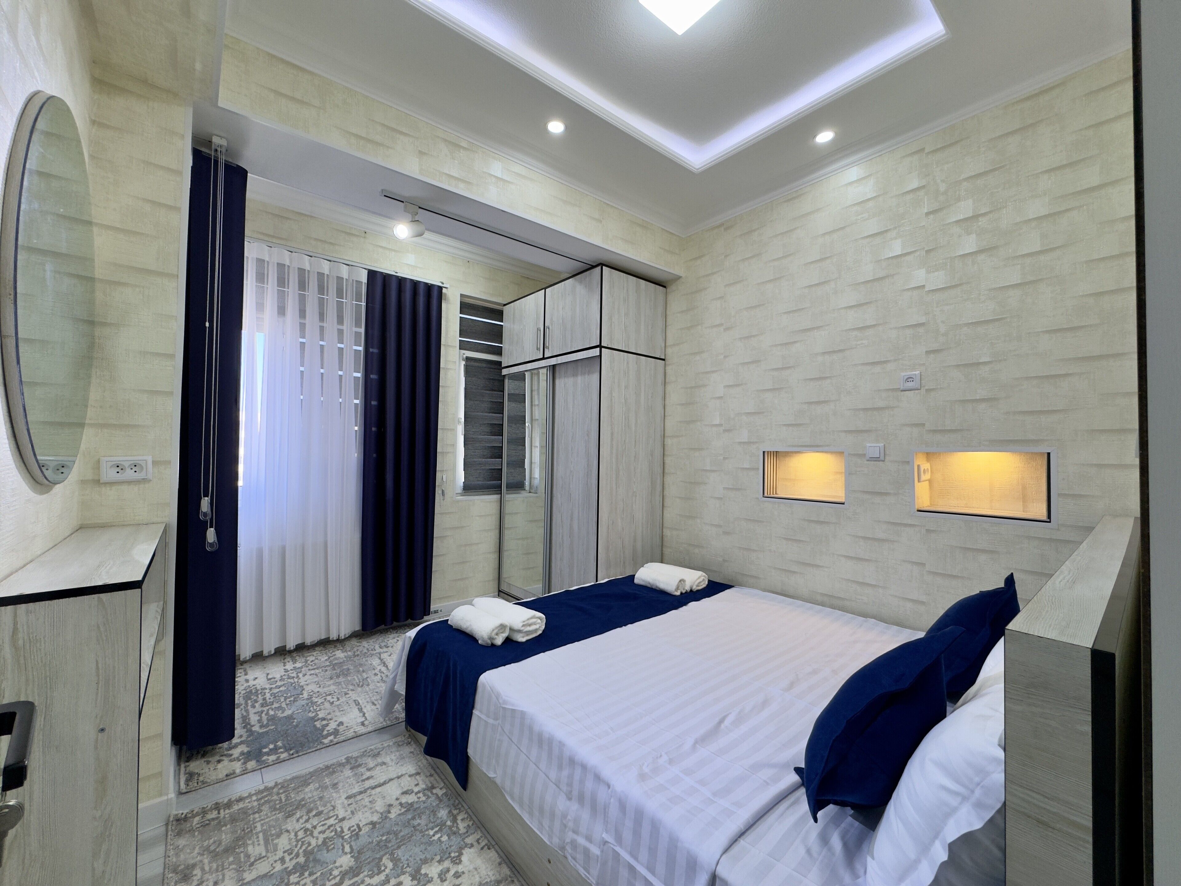 A modern hotel room with a large bed, a wardrobe, a mirror, and built-in lighting.