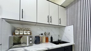 A modern kitchen with a marble countertop, black cabinets, a kettle, a coffee maker, and spice jars.