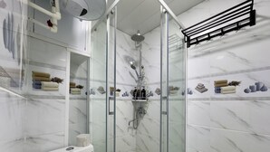 A modern bathroom with a glass-enclosed shower, marble walls, and neatly arranged towels and toiletries.