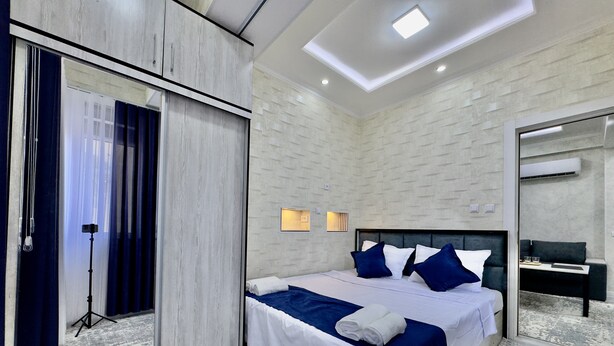 A modern hotel room with a large bed, a sliding door, a small table, and a mirror.