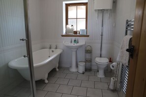 Un baño con una bañera de patas de león, un lavamanos pedestal, un inodoro y una ventana sobre el lavamanos.