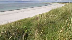 Ein Küstenstrand mit weißem Sand und einer grasbewachsenen Vordergrundfläche.