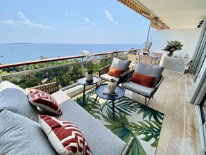 Uma varanda com sofá, cadeiras, uma mesa pequena e vista para o mar.