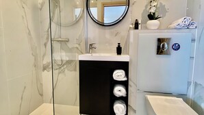 Un baño moderno con ducha de vidrio, espejo redondo, lavabo blanco y un inodoro.