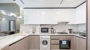 A modern kitchen with white cabinets, a built-in microwave, a gas stove, a dishwasher, and a washing machine. - StayShort - Comfortable 1BR Apartment in JVT with Gym & Pool Sleeps 2 (JVT)