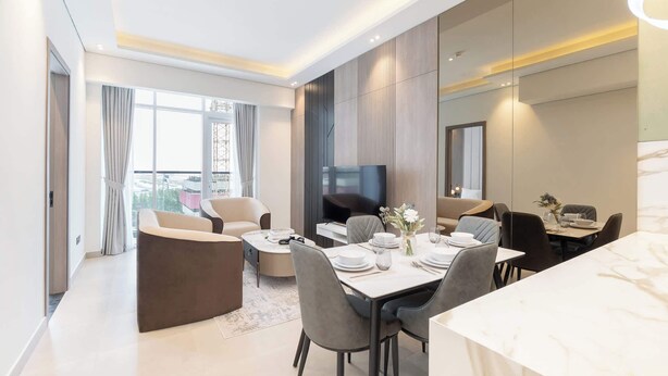 A modern dining area with a marble table, grey upholstered chairs, and a flat-screen TV. - StayShort - Comfortable 1BR Apartment in JVT with Gym & Pool Sleeps 2 (JVT)