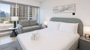 A hotel room with a bed, two bedside tables, a sofa, a large window, and a city view.