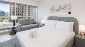 A hotel room with a bed, two bedside tables, a sofa, a large window, and a city view.